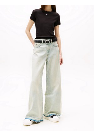 Personne portant un haut noir ajusté à manches courtes, un jean large délavé clair avec des ourlets effilochés, une ceinture noire et des baskets plateforme blanches.