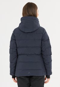 Marineblaue Pufferjacke mit Kapuze, ausgestattet mit einem gesteppten Design, glatter Textur und einem Logo am Saum. Elastische Bündchen und eine taillierte Form.