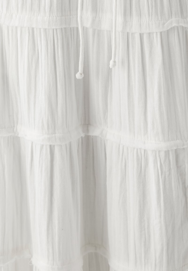 Weißes, gestuftes Kleid aus leichtem Stoff mit gekräuselter Textur. Verfügt über einen Kordelzug in der Taille und sichtbare Nahtdetails.