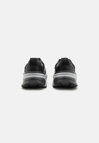 Scarpe sportive nere con tessuto testurizzato e sovrapposizioni sintetiche. Presentano un tallone arrotondato e una suola intermedia bianca con un'unità d'aria visibile.