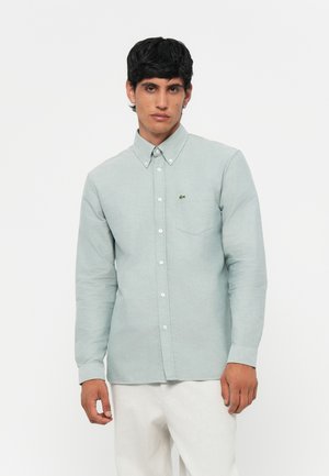Light green, button-up shirt with long sleeves, a pocket on the left, and a small embroidered logo. Smooth fabric and classic design.