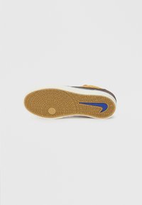 Talpa de teniși maro și galbeni, cu o suprafață texturată din cauciuc de tip gumă. Prezintă un logo Nike albastru și un model zigzag pentru aderență.