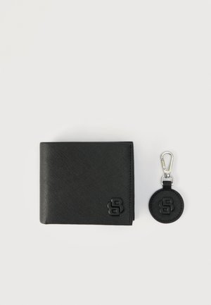 Čierna peňaženka z textúrovanej kože a okrúhly prívesok na kľúče so striebornou sponou, oba s vyrazeným štylizovaným logom "B", na svetlom pozadí.