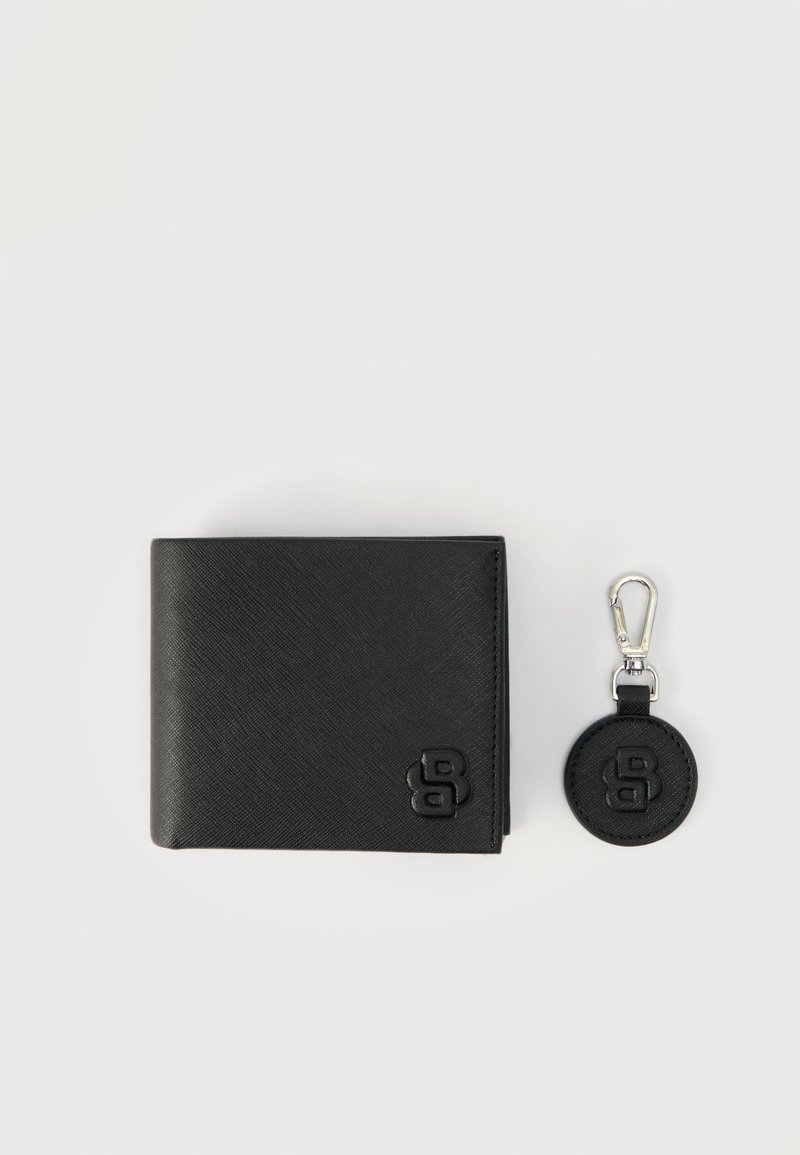 Μαύρο πορτοφόλι από υφή δέρματος και στρογγυλό μπρελόκ με ασημένια κλιπ, και τα δύο με ανάγλυφο στυλιζαρισμένο λογότυπο "B", σε φωτεινό φόντο.