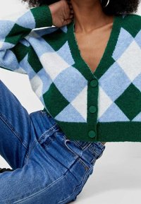 Green and light blue argyle-patterned cropped cardigan with a V-neck, featuring green buttons and ribbed cuffs. Soft knitted texture.