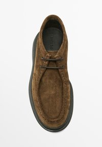 Mocassin en daim marron avec semelle noire et deux fines lacets noirs, vue de dessus sur fond blanc.