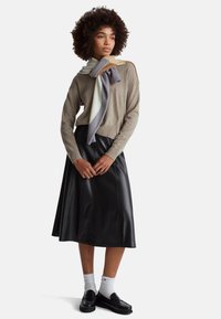 Beżowy sweter dziany, czarna skórzana spódnica midi, kolorowy szal narzucony na ramiona, czarne mokasyny, białe skarpetki, kręcone włosy, neutralne tło.