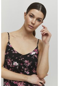 Camisole negru cu motive florale, având modele de flori roz și albe, bretele subțiri și un decolteu în V. Material ușor, neted, cu o croială lejeră.