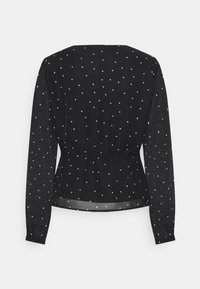 Blouse noire à manches longues avec une taille cintrée, ornée de pois blancs et de manches transparentes. Tissu lisse avec un dos froncé.