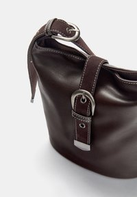 Braune Lederhandtasche mit einer weichen Textur, breiter Öffnung, silbernen Hardware-Akzenten und einem abnehmbaren Wildlederriemen.