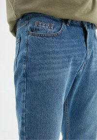 Jeans azzurri chiari in denim con una superficie liscia, caratterizzati da un classico design a cinque tasche e cuciture visibili lungo le cuciture.