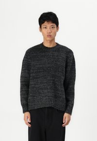 Pull en laine épaissie de couleur gris foncé avec un motif texturé, col rond et poignets côtelés. Ajustement détente, à associer avec un pantalon noir.