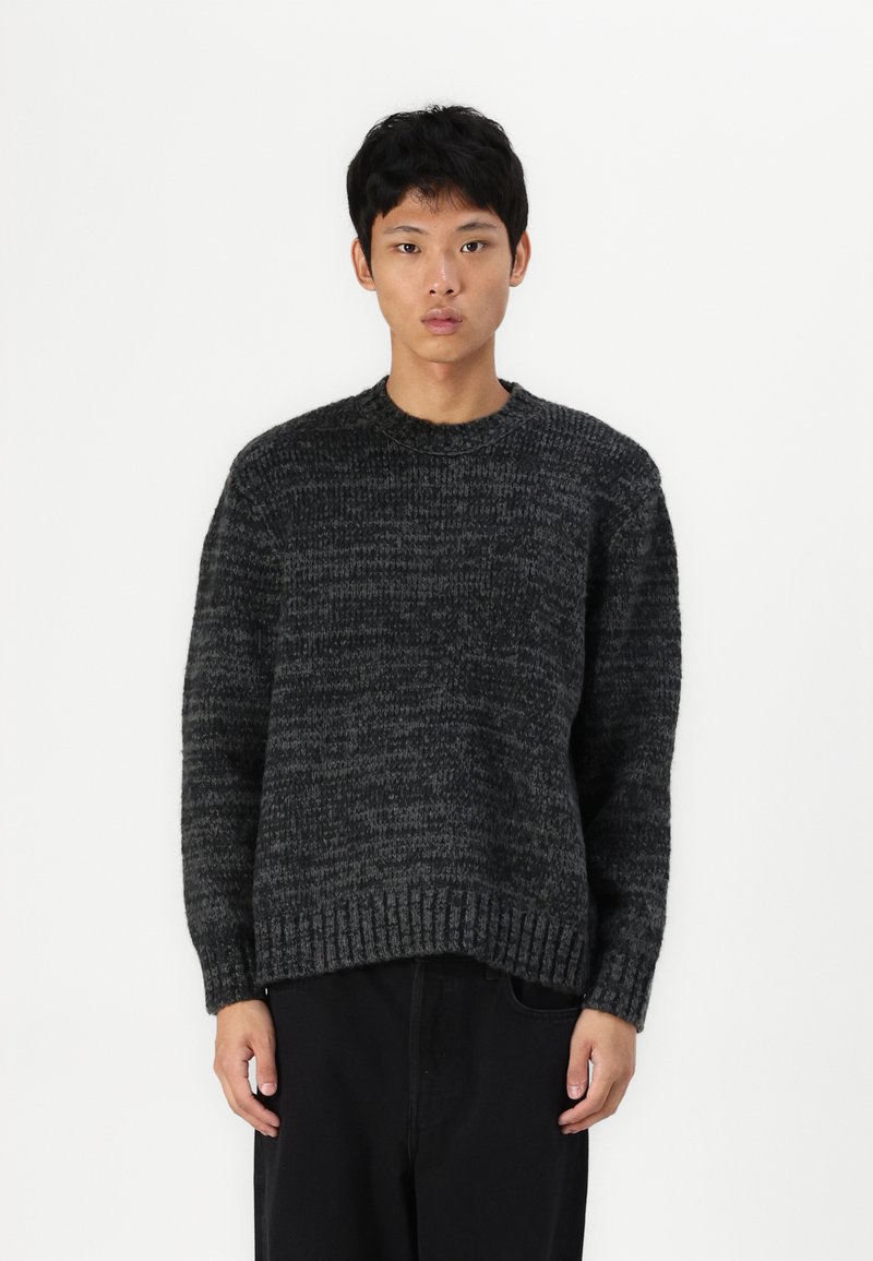 Pull en laine épaissie de couleur gris foncé avec un motif texturé, col rond et poignets côtelés. Ajustement détente, à associer avec un pantalon noir.