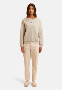 Sudadera gris con la inscripción "COOL CLUB" en letras negras, combinada con pantalones beiges y zapatillas beiges; ajuste relajado, tejido suave.