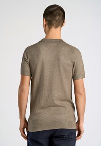 Polo de punto marrón de manga corta con cuello y dobladillo acanalados. Textura suave, diseño ajustado y patrón sutil en toda la prenda.