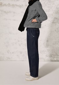 Gray textured jacket with a cropped design, paired with dark blue straight-leg jeans and white sneakers. Black knitted scarf adds contrast.