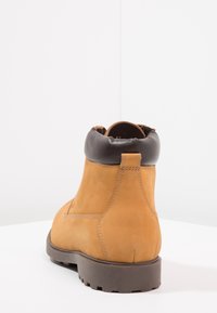 Bottine en cuir marron clair avec col rembourré marron foncé, bout rond, coutures renforcées et semelle en caoutchouc texturée. Design minimaliste.