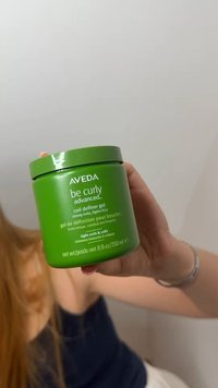 Käsi pitää vihreää purkkia Aveda Be Curly Advanced -kiharoiden muotoilugeeliä, joka tarjoaa vahvan pidon ja pörröisyyden hallinnan tiukoille kiharoille ja kierteille, 250 ml.