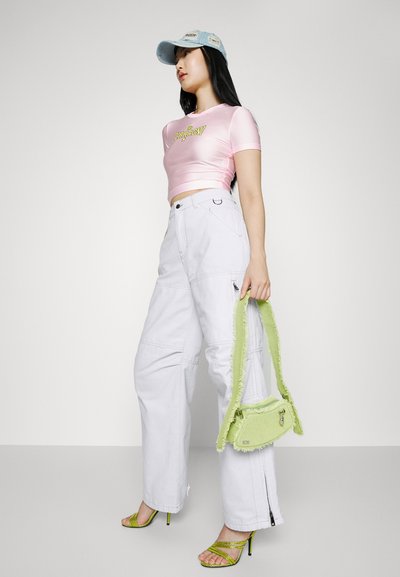Ροζ κοντομάνικο μπλουζάκι με λογότυπο, λευκά cargo παντελόνια, φωτεινή πράσινη τσάντα με τρίμματα στις άκρες και ψηλοτάκουνα σανδάλια σε πράσινο χρώμα. Απαλό φόντο.