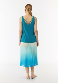 Turkusowy top na ramiączkach z krzyżującymi się paskami z tyłu, w połączeniu z plisowaną spódnicą przechodzącą od jasnego kremu do niebieskiego, kończącą się powyżej kostek.