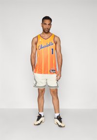 Basketbalový dres v oranžovom gradiente s modrým textom "Charlotte", doplnený o biele šortky s čiernymi akcentmi a čierne tenisky.