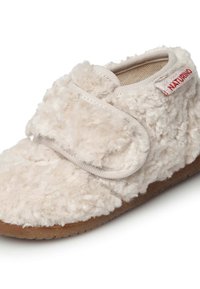 Beige plyšová šlapka s měkkou strukturou, se zapínáním na suchý zip a hnědou gumovou podrážkou. Doplňková malá červená nášivka.