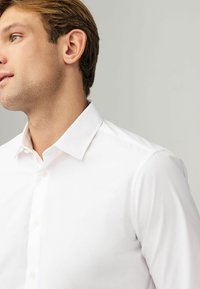 Chemise en coton blanc à boutons avec un col classique, texture lisse et éclat discret. Dotée de boutons standards à l'avant.
