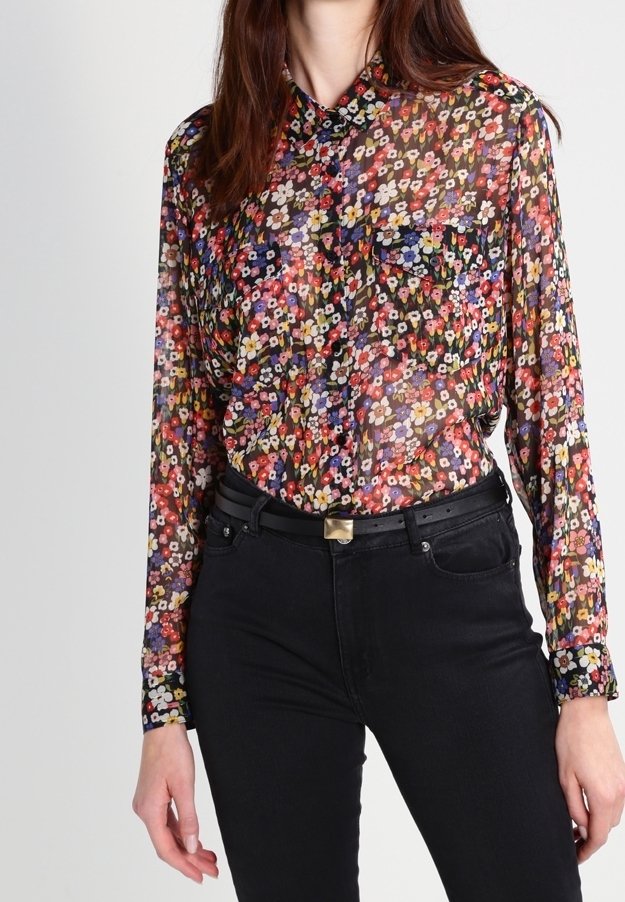 Transparent blus med ett livfullt blommönster i rött, gult, lila och blått, med en krage och en enkel bröstficka. I sällskap med svarta jeans.