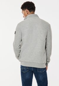 Gray sweatshirt with a high collar, made from a soft material. Paired with dark denim jeans featuring back pockets and stitching details.
