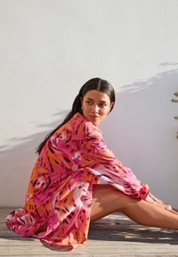 Robe vibrante et fluide aux nuances de rose et d'orange avec un motif pictural. Manches longues et coupe décontractée qui mettent en valeur la texture légère du tissu.