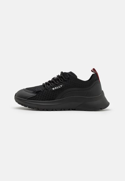 Sneakers atletici neri caratterizzati da una parte superiore in rete, suola in gomma, design con lacci e un accento rosso sul tallone. Branding visibile di lato.