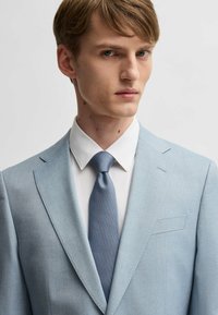 Light blue suit jacket with notched lapels and a single chest pocket, paired with a white shirt and textured blue tie. Smooth fabric finish.