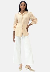 Camicia button-up di un leggero pesca con texture e colletto, abbinata a pantaloni bianchi a gamba larga e décolleté color nude.