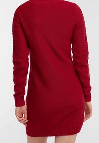 Robe tricotée rouge à manches longues, avec un col côtelé et un ourlet. Texture lisse avec une coupe ajustée, atteignant la longueur mi-cuisse.