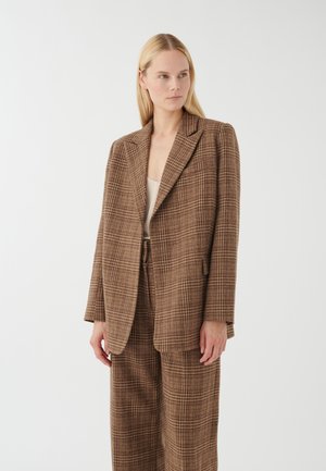 Hnedý károvaný oversize blazer s výrezom na golieri, jedným gombíkom na zapínanie a prednými vreckami, v kombinácii s nohavicami s širokými nohavicami.