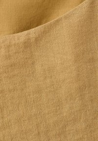 Gros plan d’un tissu beige texturé avec motif tissé visible et fibres naturelles dans une disposition souple et pliée.