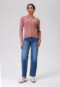 Rožinė šonkačių rašto megztinis su apykakle, su sagomis priekyje, derinamas su mėlynomis tiesiomis kelnėmis ir šviesiais sportbačiais. Smulkus paviršius, laisvas tinkas.