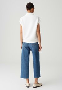 Top corto bianco a maniche corte con tessuto testurizzato, abbinato a jeans a vita alta e gamba larga di un blu chiaro e scarpe beige senza lacci.