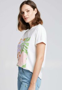 T-shirt en coton blanc à manches courtes, présentant un grand motif floral en rose, vert, orange et violet. Coupe légèrement décontractée.