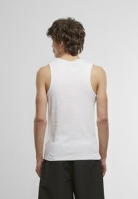Weißes Baumwoll-Tanktops mit rundem Halsausschnitt und ärmellosem Design. Glatte Textur, einfarbiger Stoff, getragen mit dunklen Shorts.