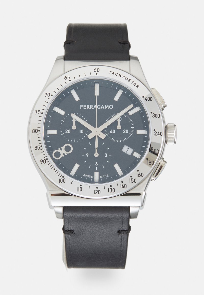 Sudraba nerūsējošā tērauda pulkstenis ar tumši zilu ciparnīcu, baltām indeksēm, hronogrāfa funkcijām un melnu ādas siksniņu. Uzsvērts ar taksimetru.