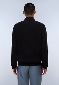 Maglione nero lavorato a maglia con colletto alto, maniche lunghe e orlo aderente. Tessuto testurizzato, mostrato di schiena su uno sfondo chiaro.