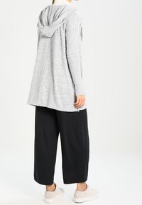 Grå, texturerad huvtröja med huva, i kombination med svarta vida byxor och ljusgrå sneakers. Outfiten betonar komfort och lagerdesign.