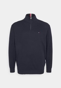Pull-over en navy avec un col haut et une demi-fermeture éclair. Poignets et ourlet côtelés. Petit logo sur la poitrine en rouge, blanc et bleu. Texture douce.
