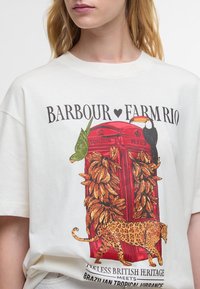 T-shirt branca de algodão com uma ilustração de uma cabine telefónica vermelha rodeada de bananas, aves tropicais e um leopardo; mangas curtas.