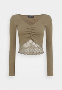 Olivgrön långärmad kort topp med V-ringning, draperad mittdel och spetsdetalj vid fållen.