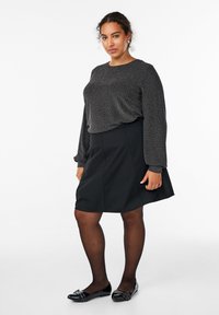 Črna krila s širšim robom, v kombinaciji z teksturiranim sivim dolgim rokavom, ki ima vzorec ribje kosti. Črne čevlje z dekorativnimi detajli.