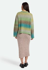 Pulover tricotat multicolor cu dungi verzi, albastre și maronii, asortat cu o fustă lungă bej și pantofi negri cu talpă groasă. Material texturat.