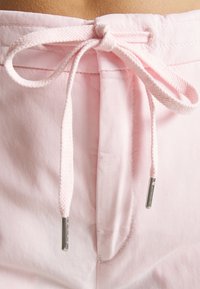 Lichtroze stoffen shorts met een verstelbare tailleband. De trekkoord heeft zilveren metalen uiteinden en een gestructureerd oppervlak.