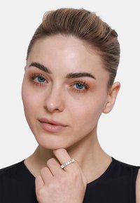 Goldfarbener Ring mit rechteckigen Edelsteinen. Glatte Textur, modernes Design. Modell trägt den Ring und berührt das Kinn.